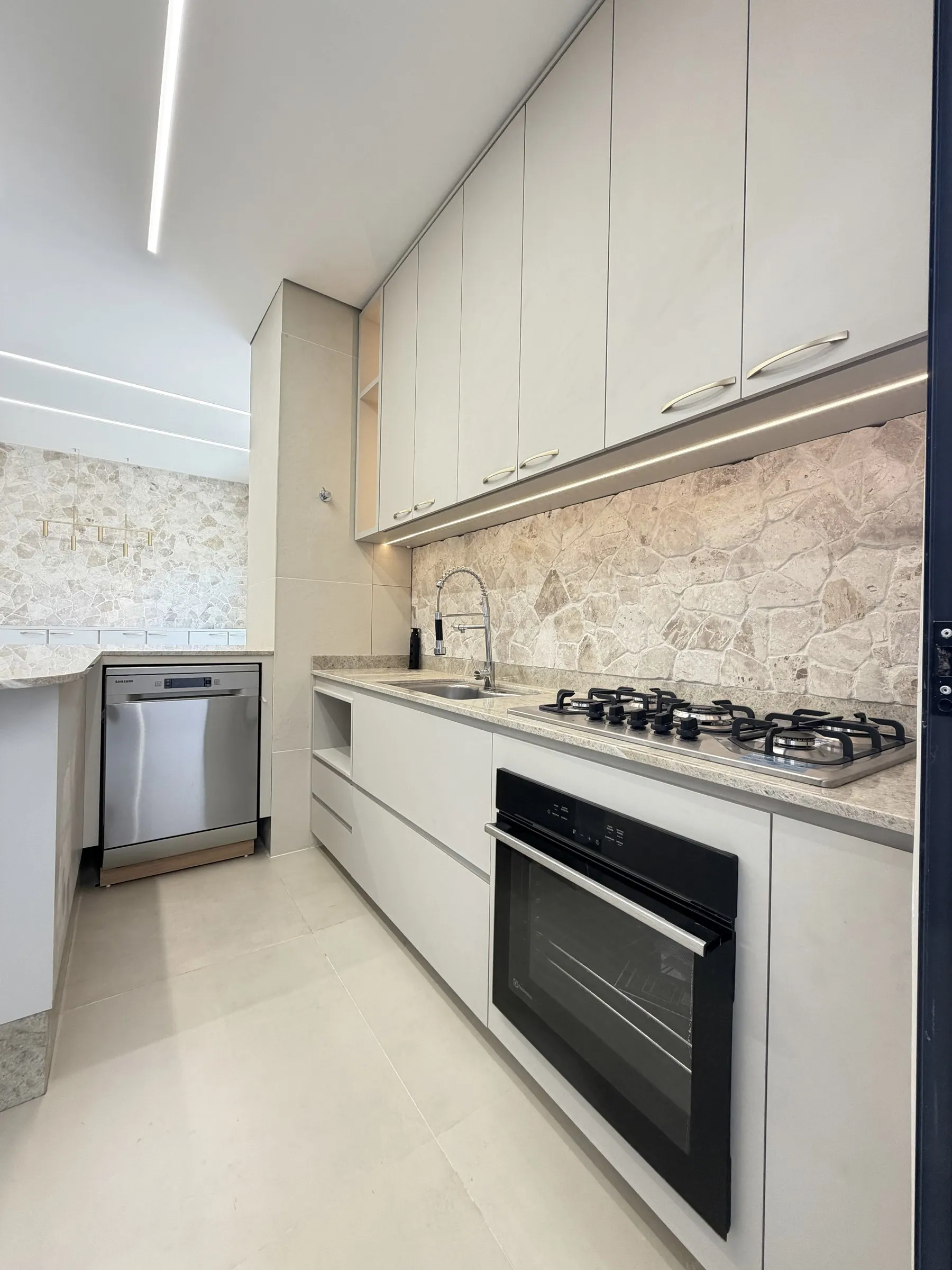 Cozinha gourmet planejada em tons claros, com bancada em pedra e revestimento de pedra natural